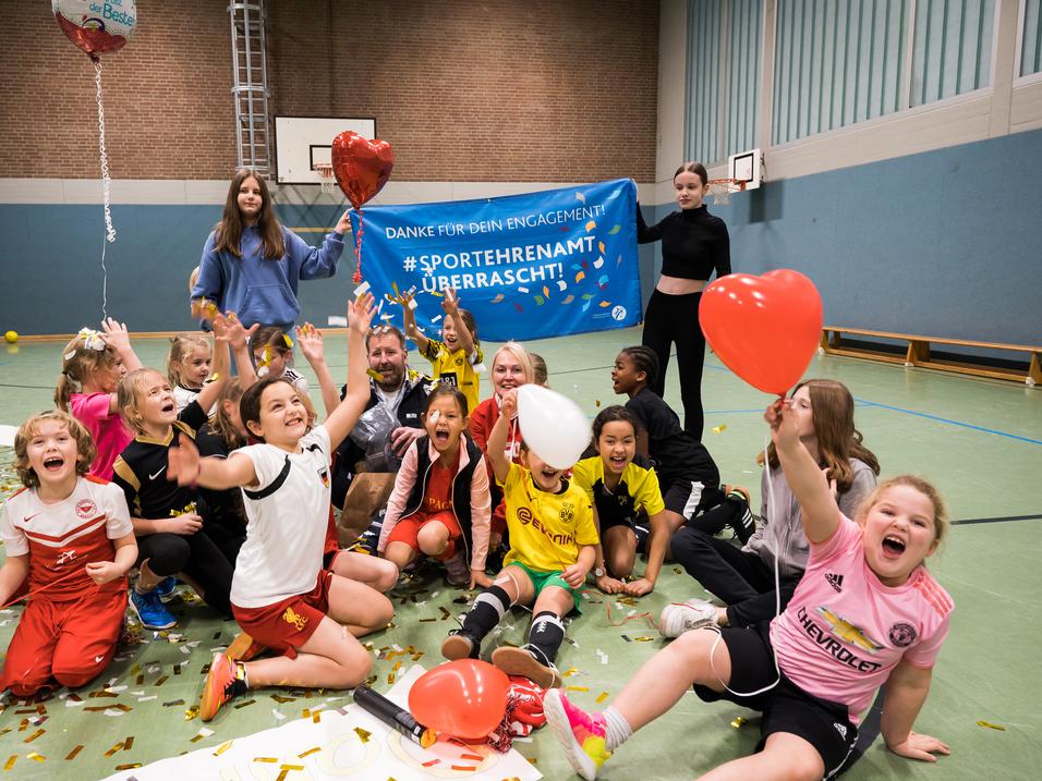 Gruppenszenen mit begeisterten Kindern in Sportkleidung, die Ballons halten und vor einem Danke-Schild feiern.