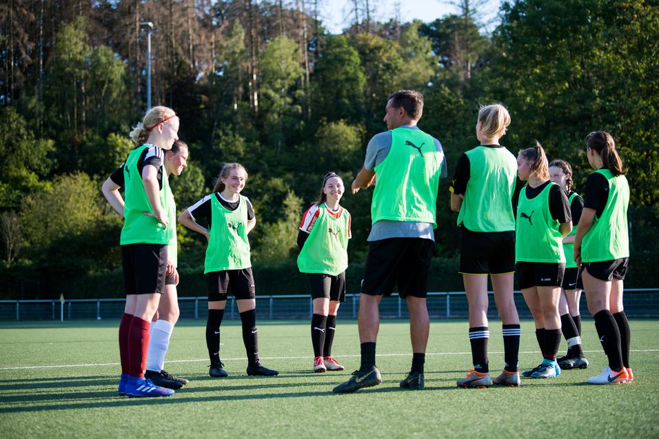 Mannschaftstraining mit Trainer: Gruppen von Mädchen tragen grüne Trainingswesten auf einem Fußballplatz.